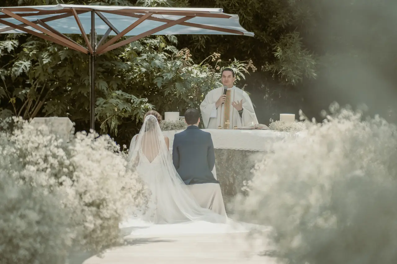Los novios de espaldas ante el altar del jardín mientras el sacerdote habla