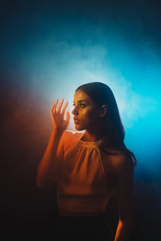 Figura entre humo azul, iluminada de frente por una luz cálida