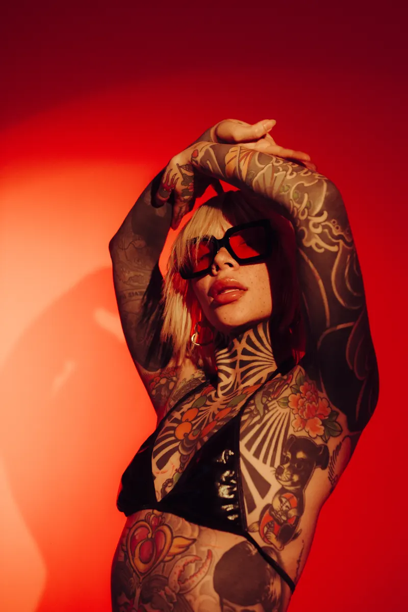 Retrato de brazos tatuados y lentes oscuros sobre un fondo rojo encendido