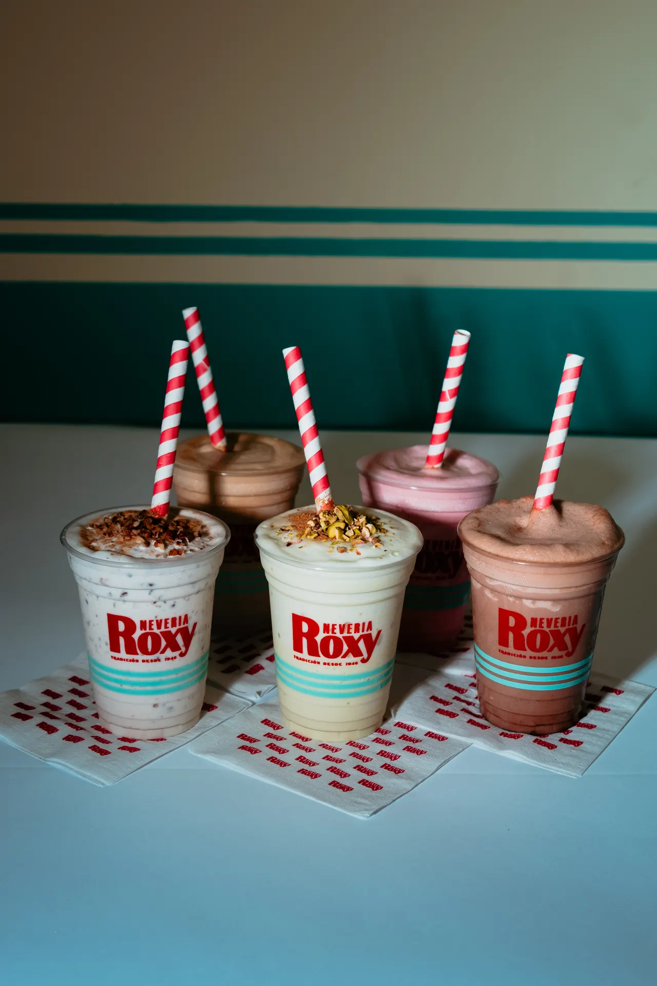 Tres malteadas de Roxy con popotes de rayas sobre la mesa del local, frente a la pared turquesa