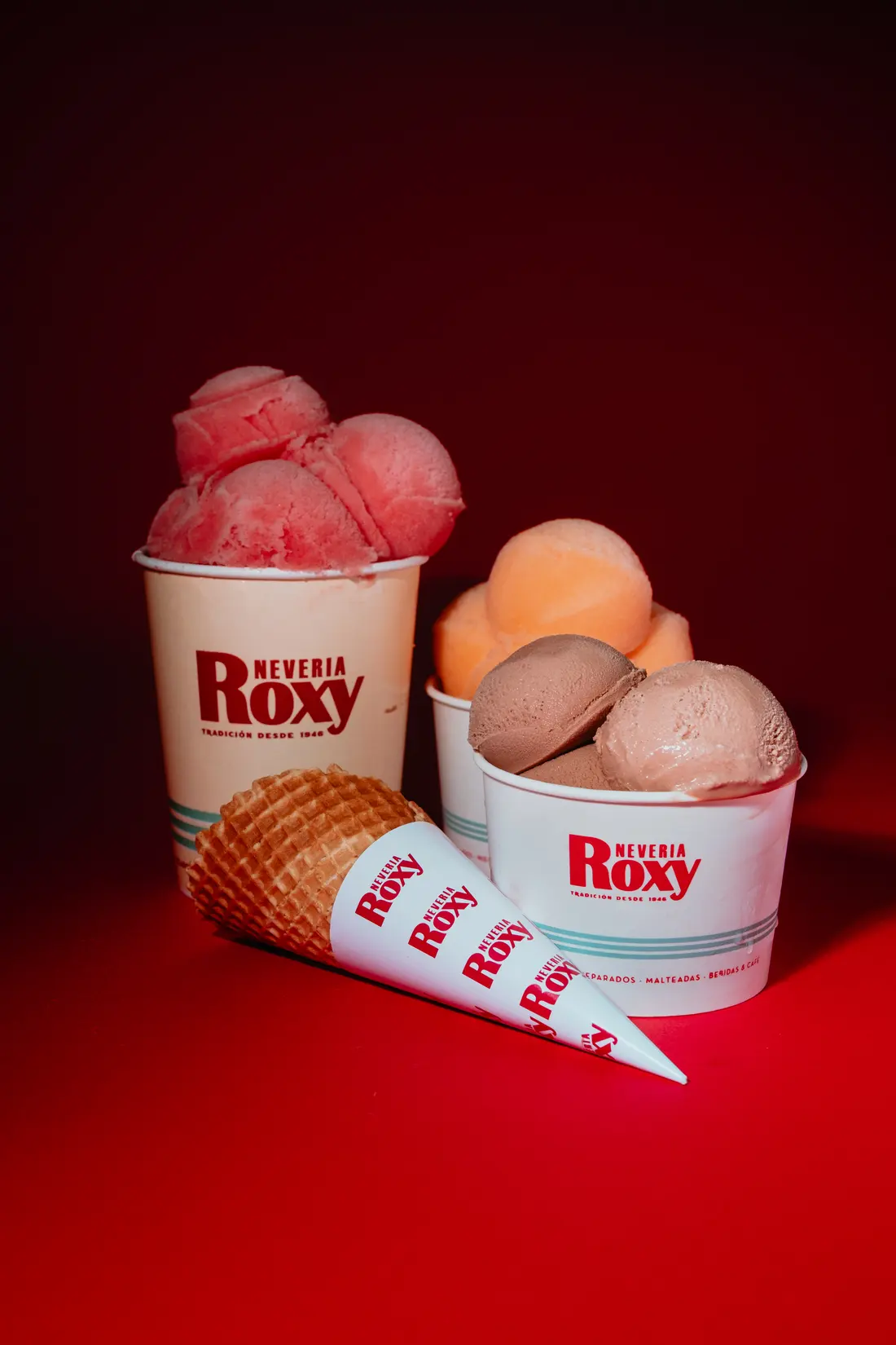 Botes y conos de Roxy con bolas de fresa, mango y chocolate sobre fondo rojo