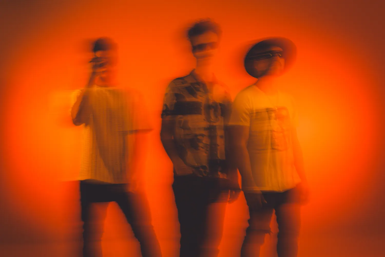 Los tres músicos barridos por el movimiento sobre un fondo naranja