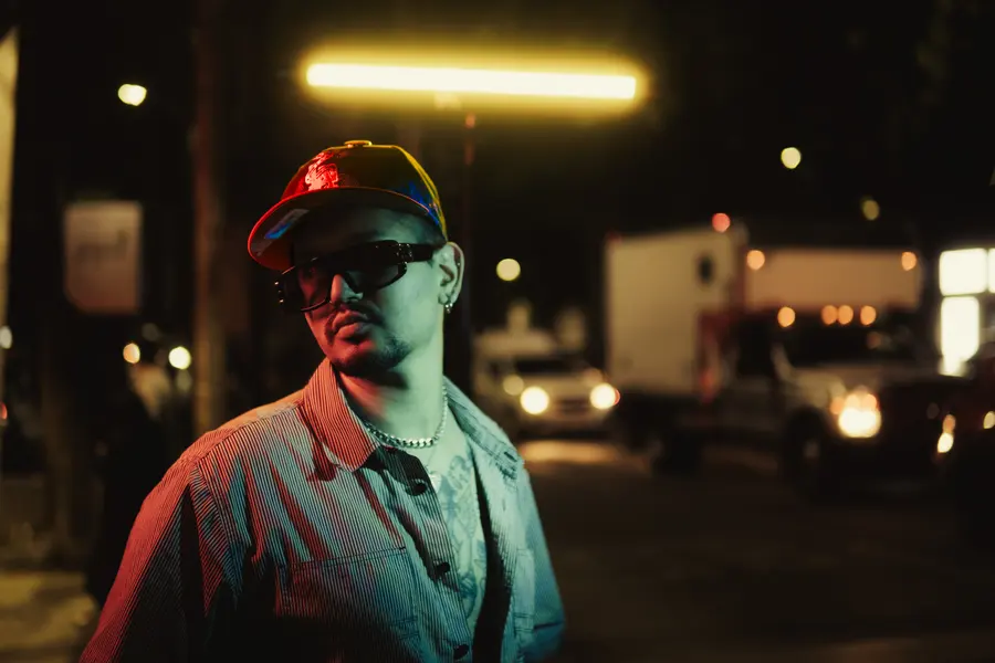 Retrato de noche, gorra puesta y lentes oscuros, con los faros del tráfico detrás