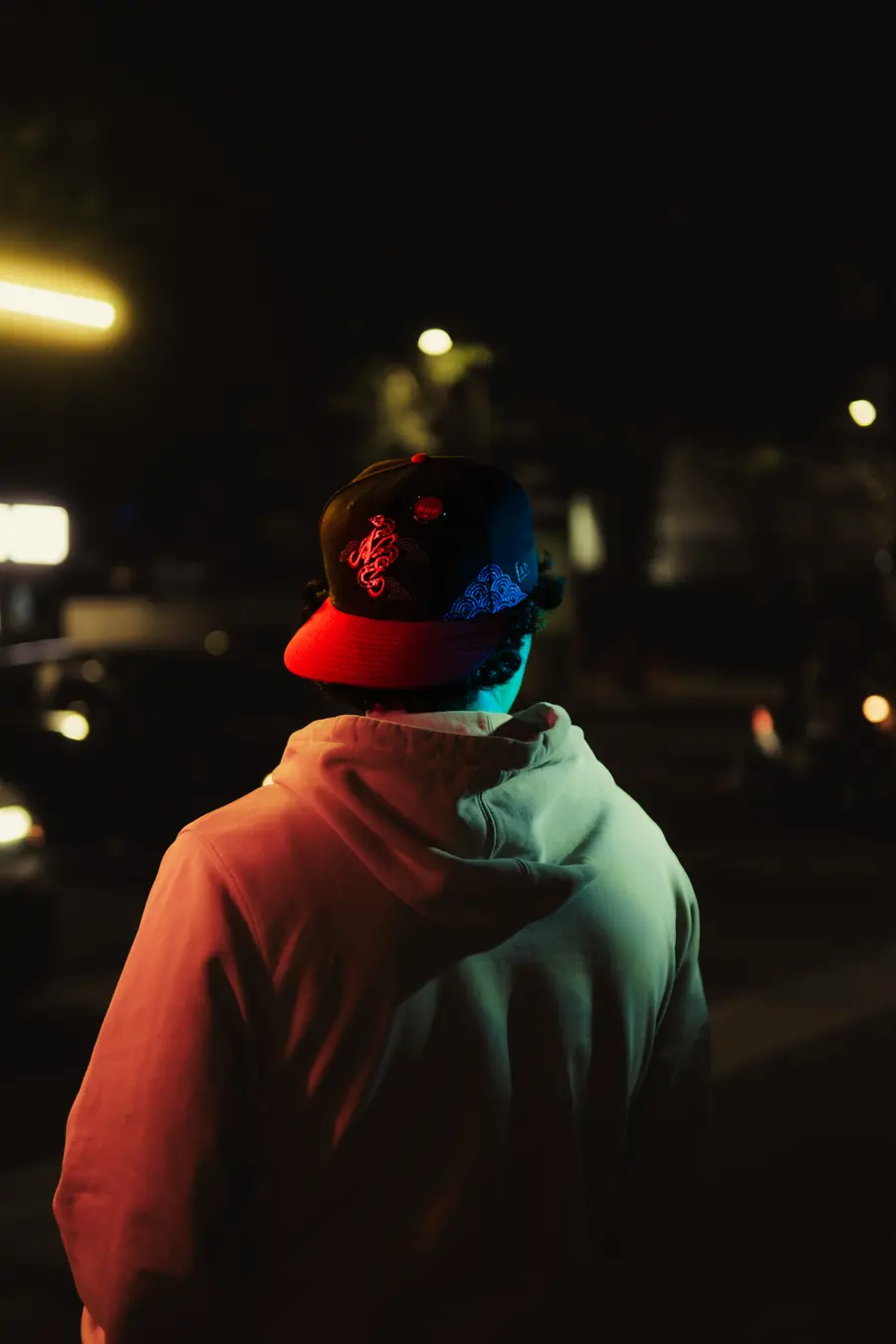 De espaldas, una gorra New Era bajo la luz de un tubo de neón en la calle
