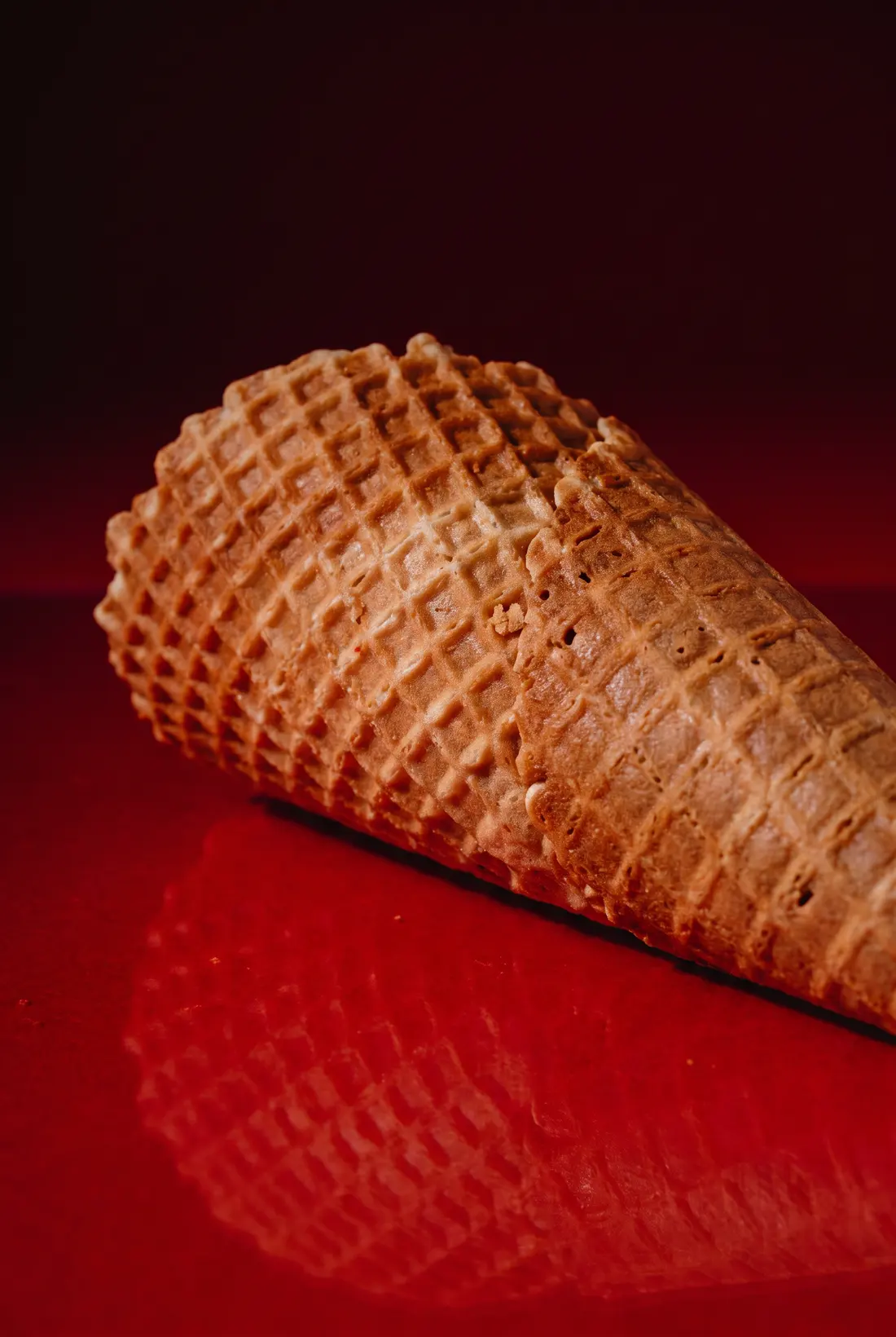 Un barquillo de galleta recostado sobre una superficie roja brillante