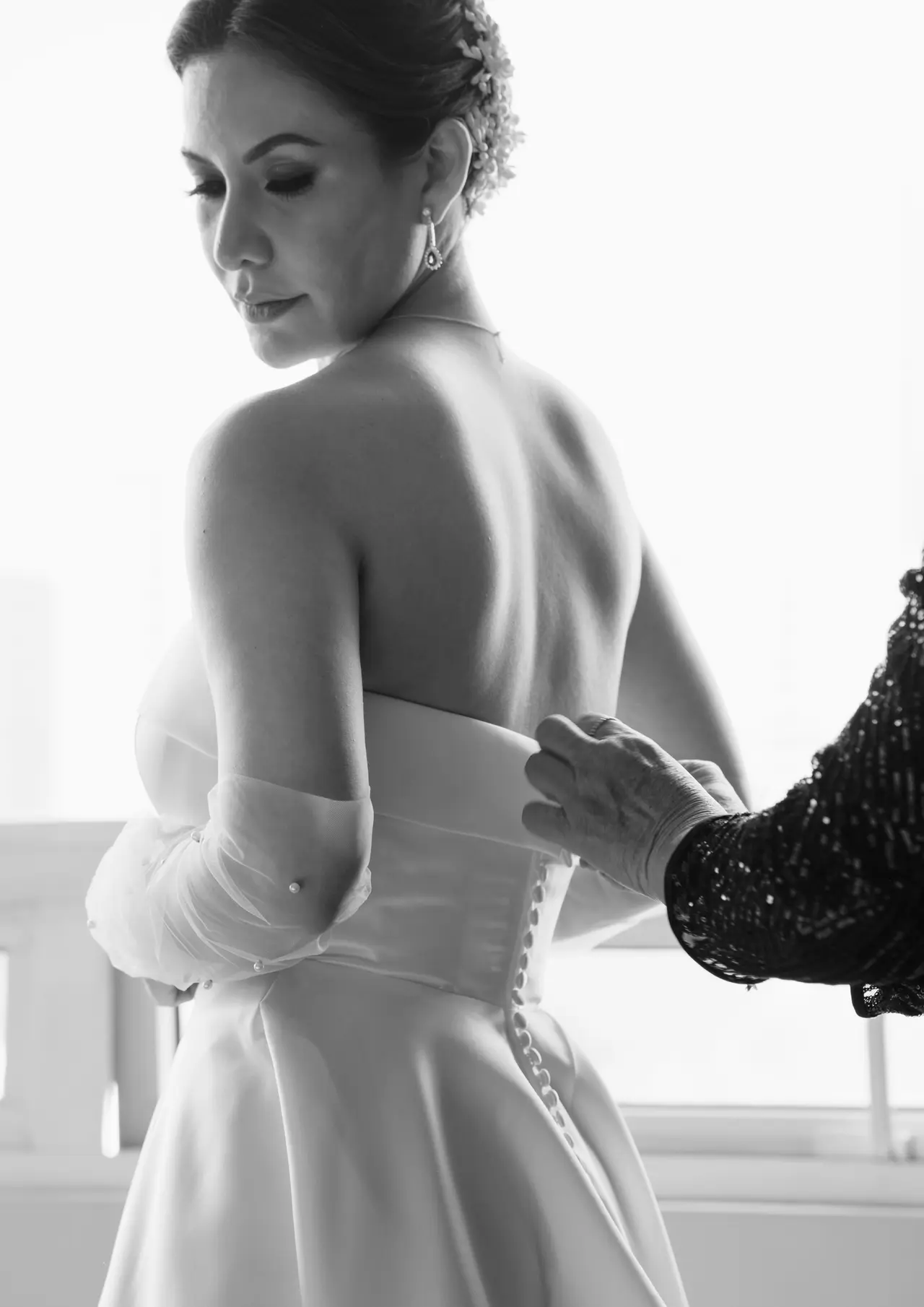 Las manos de alguien abrochan el vestido en la espalda desnuda de la novia, en blanco y negro