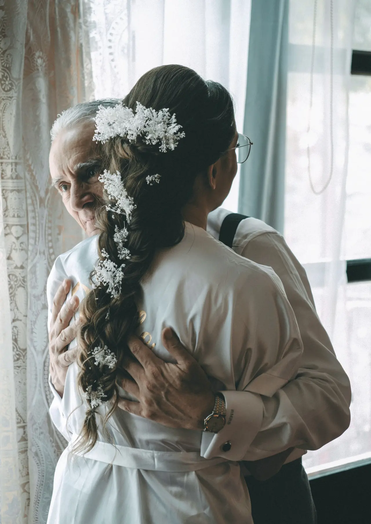 La novia abrazada a su padre, con flores en el pelo, a contraluz